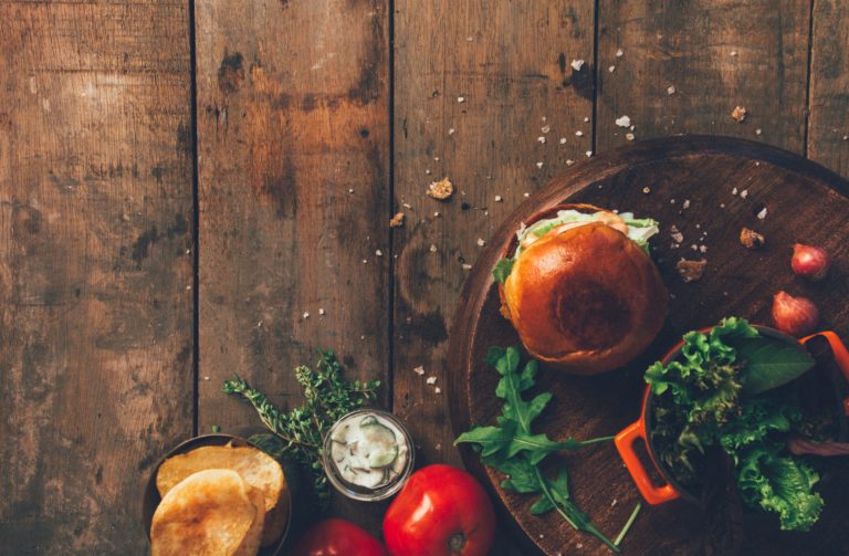 burger-and-vegetables-placed-on-brown-wood-surface-1565982